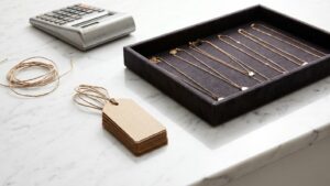 Gold-toned wholesale necklaces on a charcoal velvet tray beside blank kraft price tags and a calculator on marble
